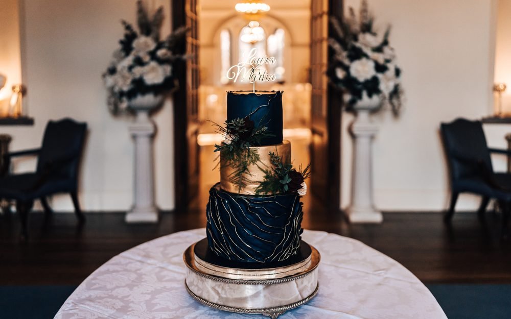 A tiered wedding cake with gold and greenery detail