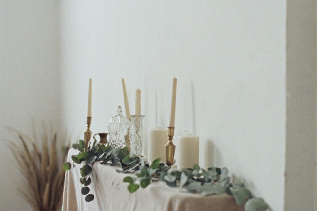 Beeswax candles of different heights in mismatched brass and glass holders on linen