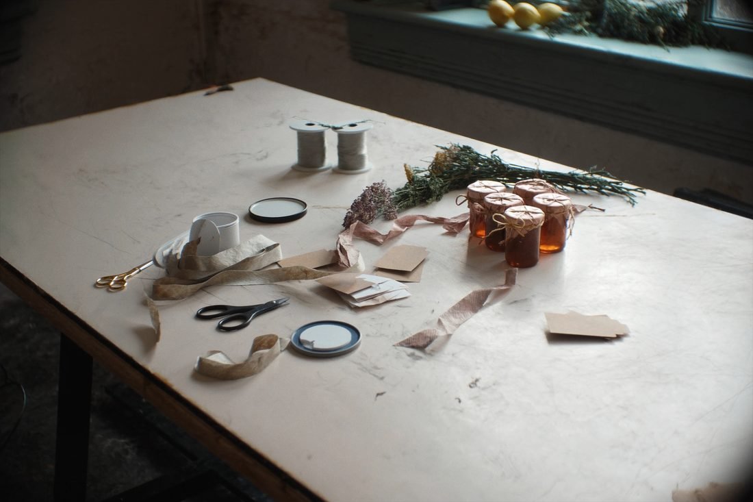 A craft table part way through the work, with ribbon, paper tags and jars being wrapped in twine