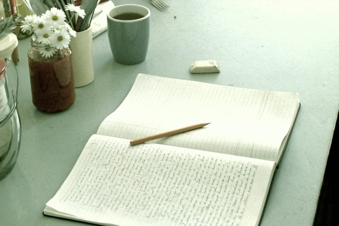 A ruled notebook open on a kitchen table showing a long handwritten list