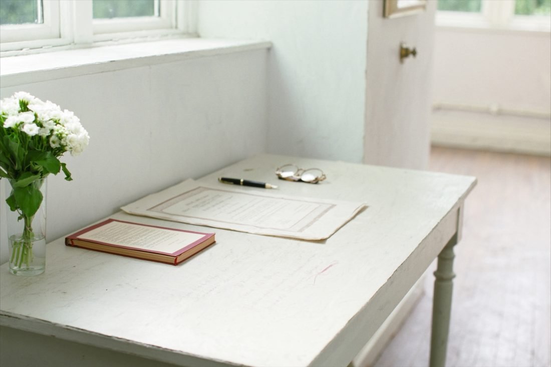 Wedding paperwork on a limewashed table with a certificate sleeve and sweet peas