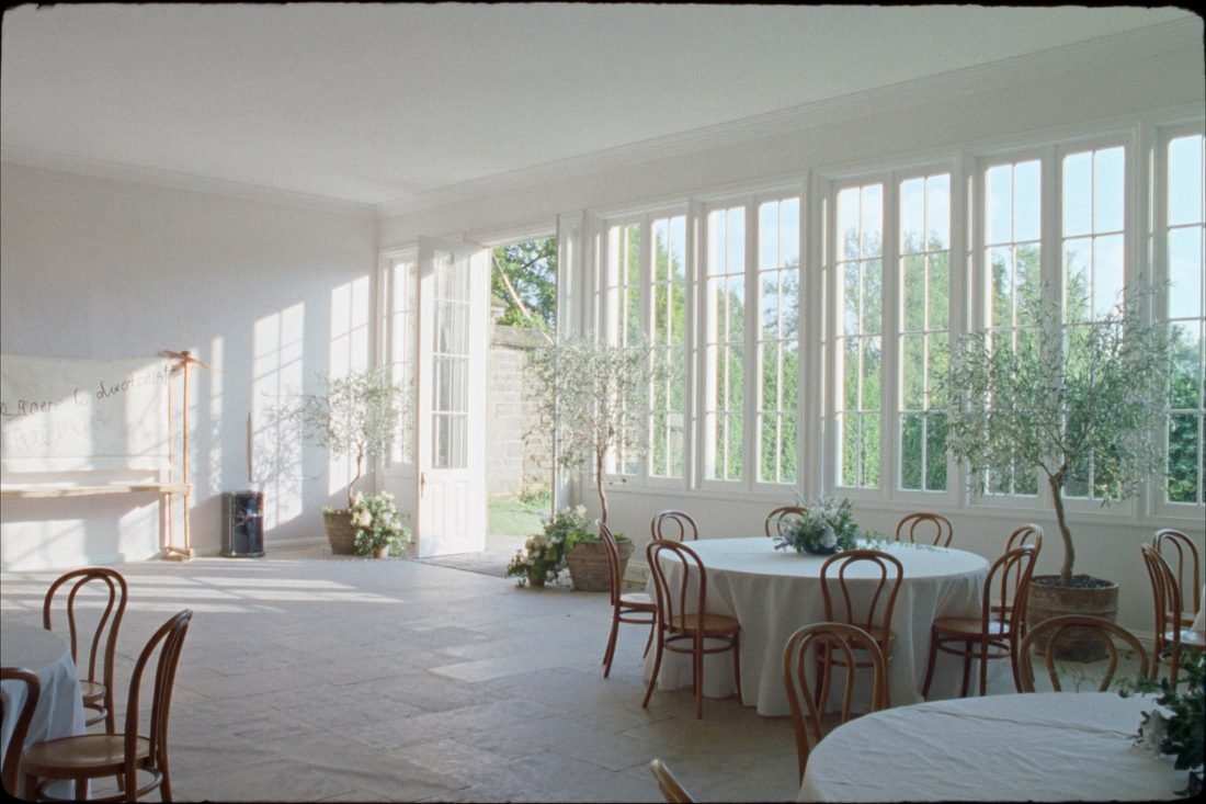 A glazed orangery laid with round tables, looking out onto the garden through full-height windows