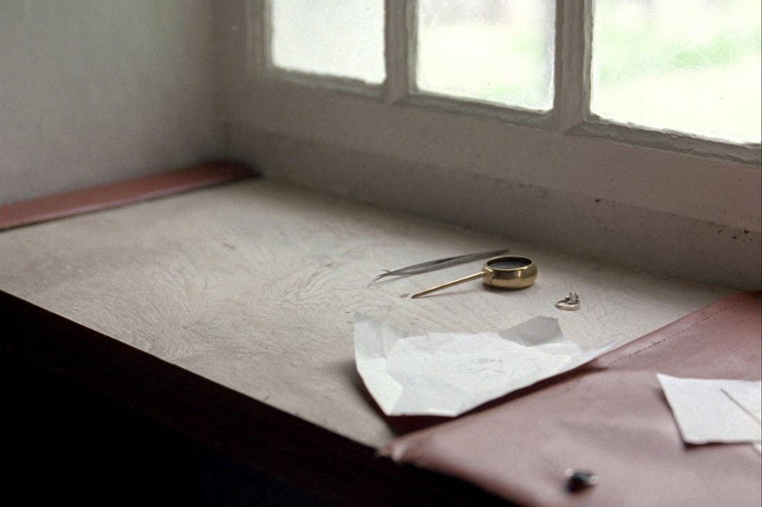 A jeweller's bench by a window with a brass loupe, tweezers and folded diamond papers