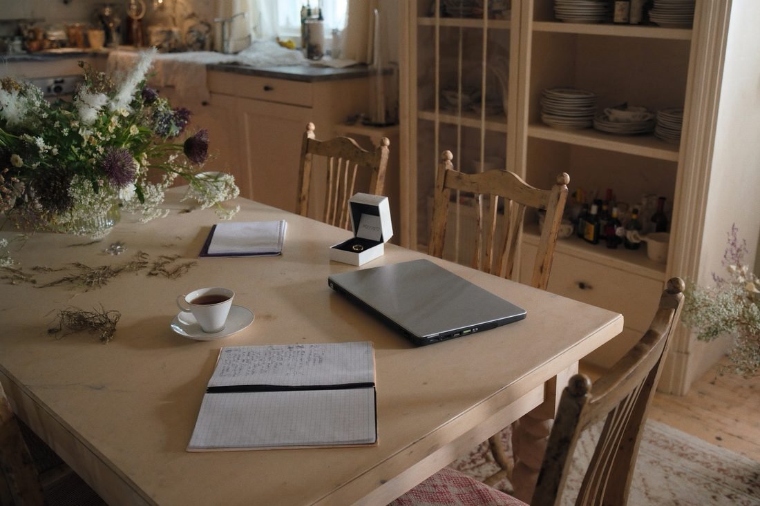A closed laptop on a farmhouse table beside an open ring box and a notebook of comparisons