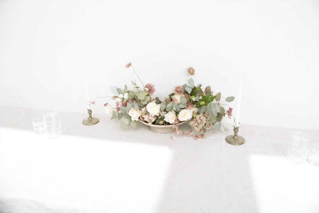 A low centrepiece of garden roses and sweet peas between small brass candlesticks