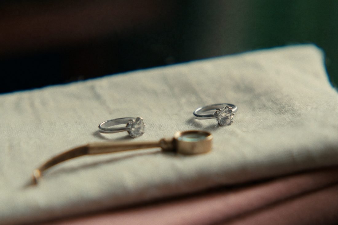 Two matching solitaire rings side by side on oat linen with a brass loupe between them