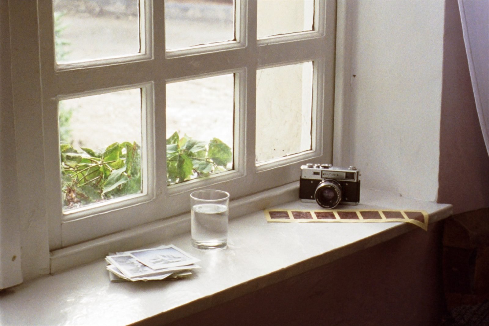An old film camera on a painted windowsill beside a strip of contact sheets