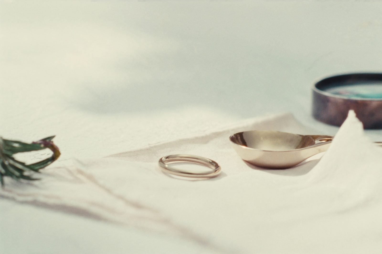 Two plain gold wedding bands resting on folded oat linen beside a small brass dish
