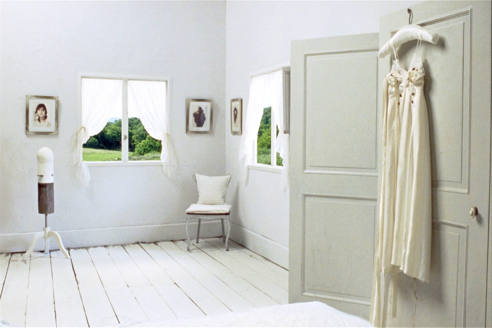 A silk wedding dress on a padded hanger on the open door of a pale painted wardrobe