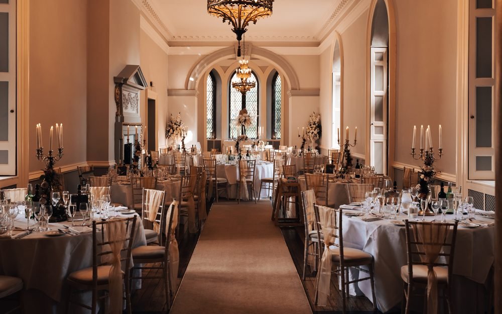 A long panelled dining room laid with round tables, opening through an arch to a further room